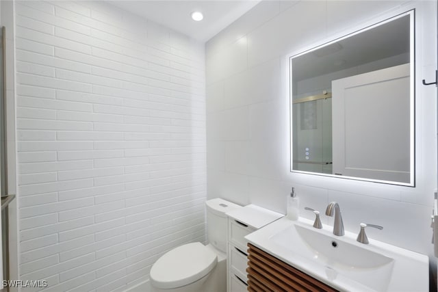 bathroom featuring tasteful backsplash, vanity, tile walls, toilet, and a shower with shower door