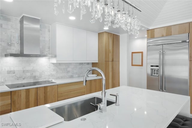 kitchen featuring white cabinets, wall chimney range hood, hanging light fixtures, and built in refrigerator