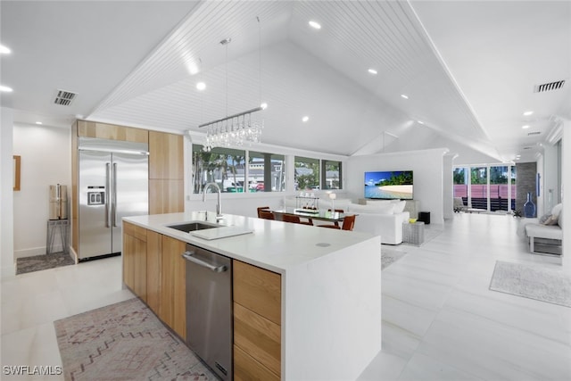 kitchen with stainless steel appliances, vaulted ceiling, sink, pendant lighting, and an island with sink