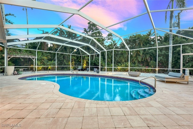 pool at dusk featuring glass enclosure and a patio area