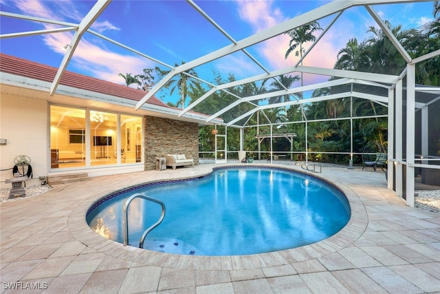 pool at dusk featuring a lanai and a patio