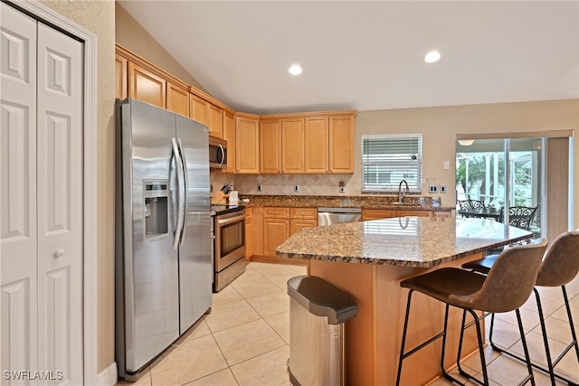 kitchen with appliances with stainless steel finishes, a kitchen breakfast bar, light stone countertops, a kitchen island, and vaulted ceiling