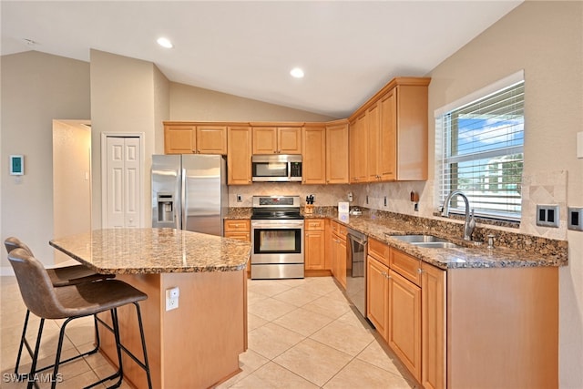 kitchen featuring sink, appliances with stainless steel finishes, dark stone countertops, a center island, and vaulted ceiling