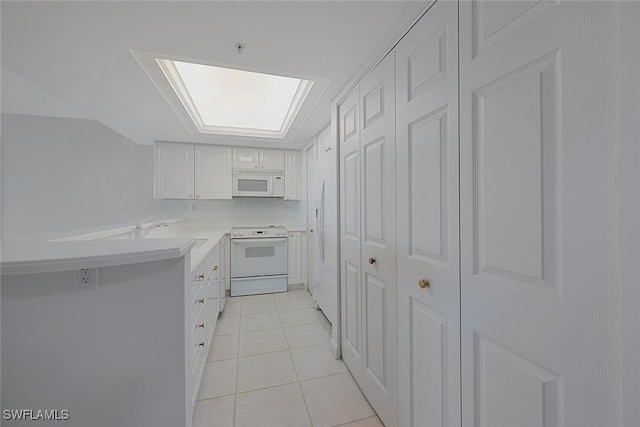 kitchen with a skylight, white cabinetry, sink, white appliances, and light tile patterned flooring