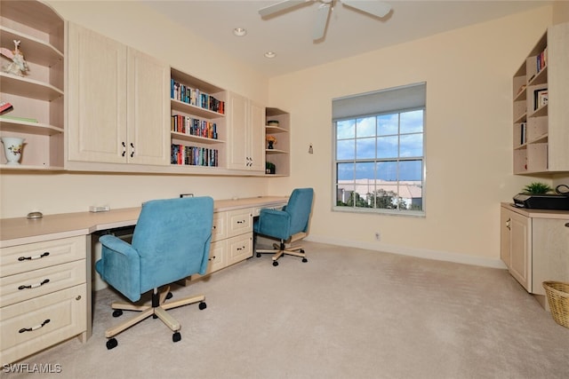 home office with light colored carpet, built in desk, and ceiling fan