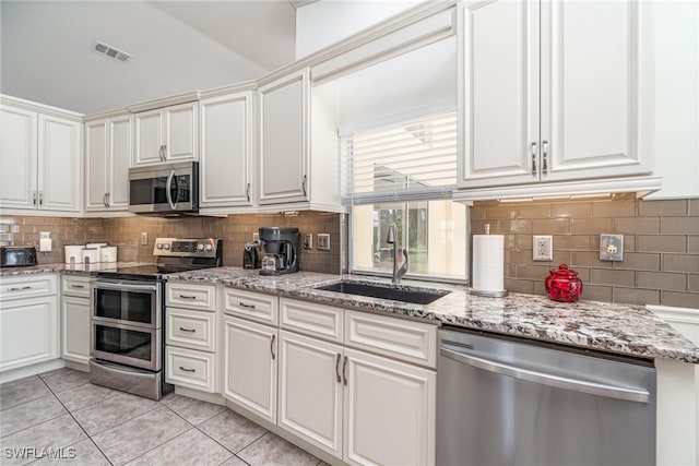 kitchen featuring tasteful backsplash, light tile patterned flooring, appliances with stainless steel finishes, sink, and white cabinets