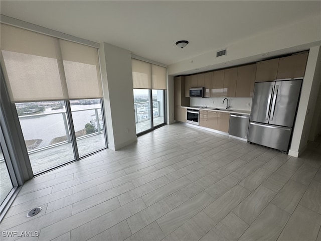 kitchen featuring appliances with stainless steel finishes, a sink, a wall of windows, light countertops, and modern cabinets