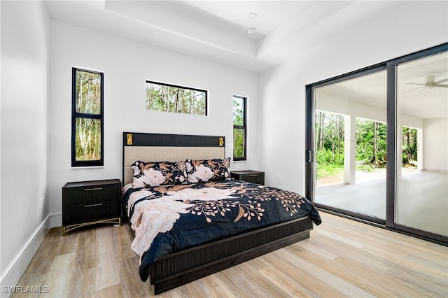 bedroom featuring light wood-type flooring, access to exterior, and a raised ceiling