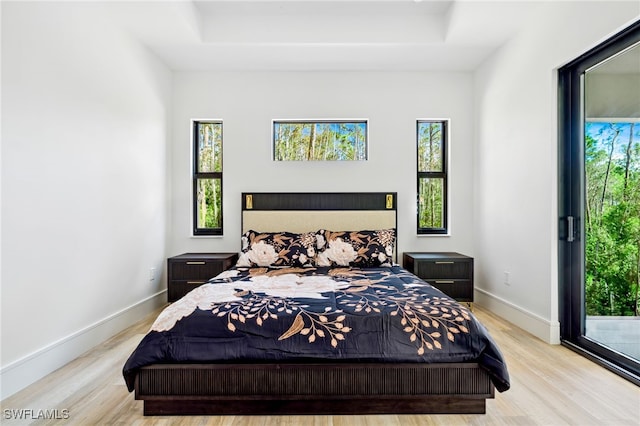 bedroom with light wood-type flooring, access to exterior, and a tray ceiling