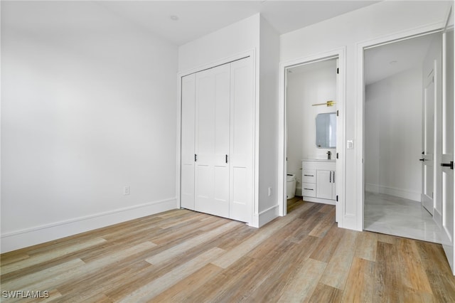 unfurnished bedroom featuring light wood-type flooring, a closet, and ensuite bath