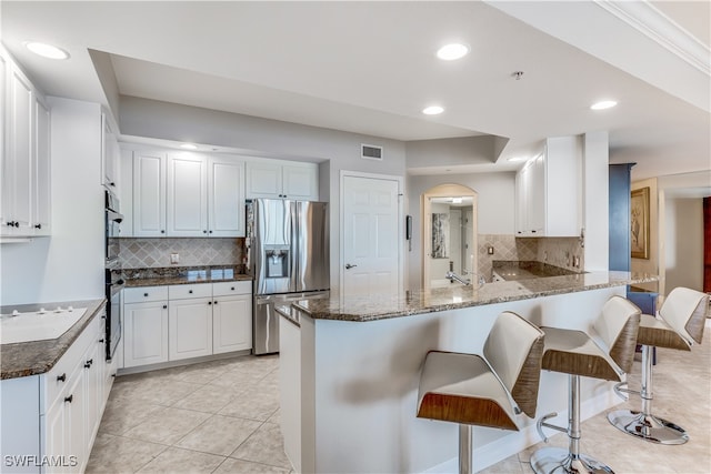 kitchen featuring white cabinetry, appliances with stainless steel finishes, a breakfast bar area, dark stone countertops, and kitchen peninsula