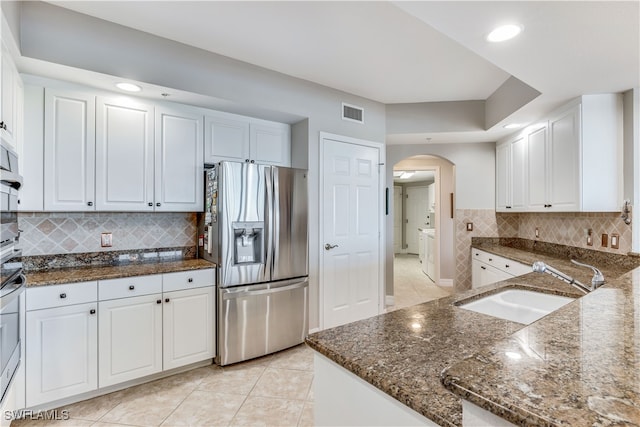 kitchen featuring stainless steel appliances, white cabinets, sink, light tile patterned floors, and dark stone countertops