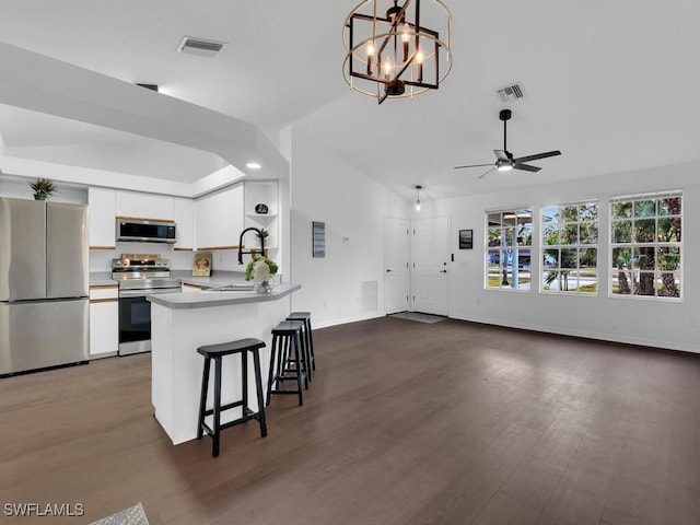 kitchen with ceiling fan with notable chandelier, kitchen peninsula, appliances with stainless steel finishes, decorative light fixtures, and white cabinetry