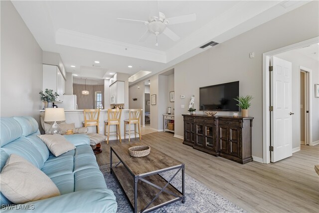 living room featuring light wood-type flooring, ceiling fan, and a raised ceiling