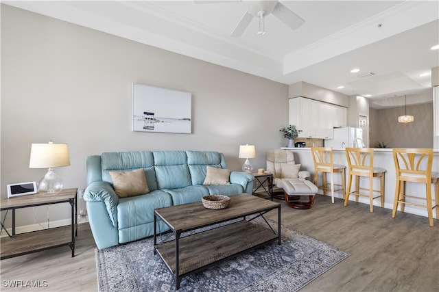 living room featuring light wood-type flooring, a raised ceiling, ceiling fan, and crown molding