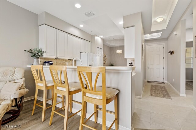 kitchen with white cabinetry, kitchen peninsula, a kitchen breakfast bar, white fridge with ice dispenser, and backsplash