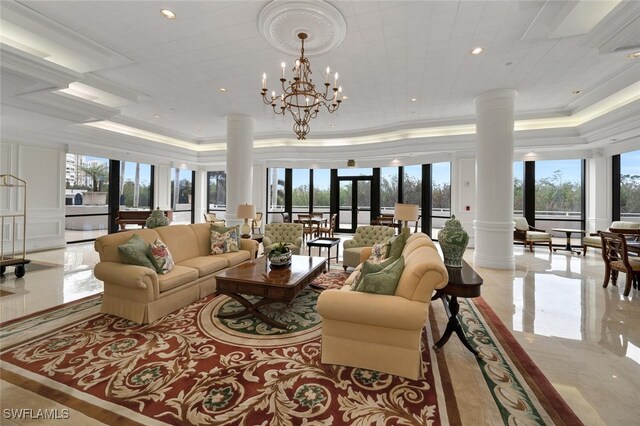 living room featuring french doors, decorative columns, a raised ceiling, crown molding, and a chandelier