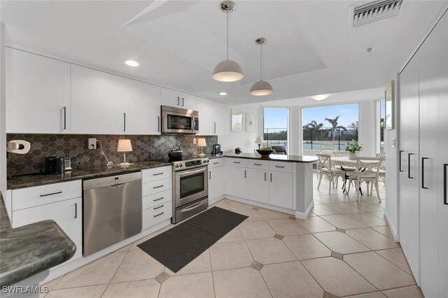 kitchen featuring white cabinets, tasteful backsplash, decorative light fixtures, kitchen peninsula, and stainless steel appliances