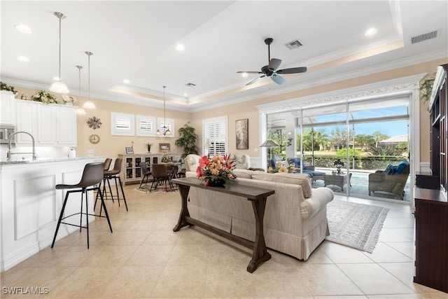 living room with light tile patterned flooring, ceiling fan, crown molding, and a tray ceiling