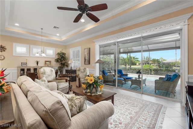 tiled living room with ceiling fan, ornamental molding, and a raised ceiling