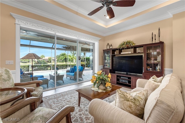 tiled living room with ceiling fan, a tray ceiling, and ornamental molding