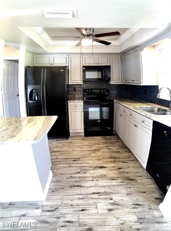 kitchen with a raised ceiling, sink, black appliances, and light hardwood / wood-style floors