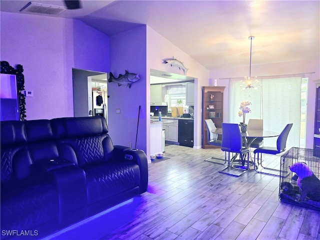 living room featuring light wood-type flooring, vaulted ceiling, and a notable chandelier