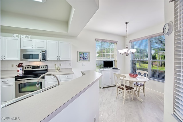 kitchen featuring stainless steel appliances, light hardwood / wood-style floors, hanging light fixtures, white cabinets, and decorative backsplash