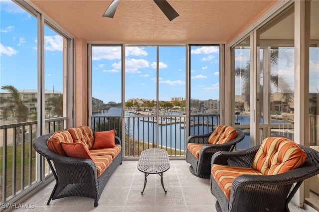 sunroom with ceiling fan and a water view