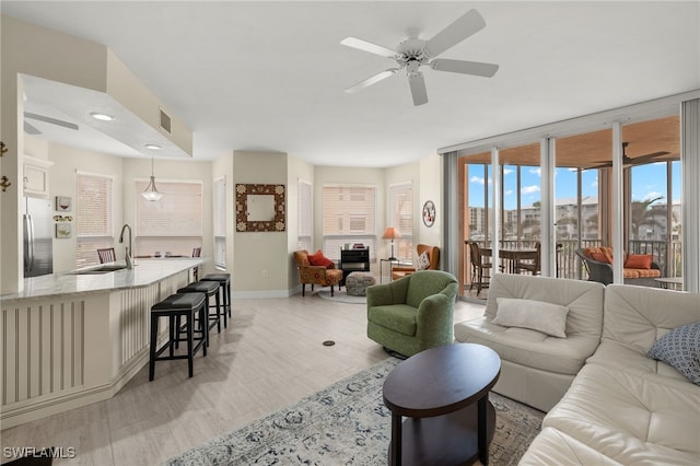 living room featuring expansive windows, ceiling fan, sink, and light wood-type flooring