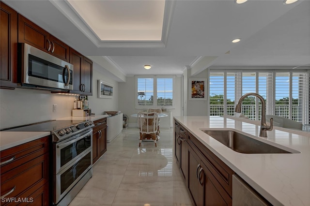 kitchen featuring sink, ornamental molding, a raised ceiling, light stone countertops, and appliances with stainless steel finishes