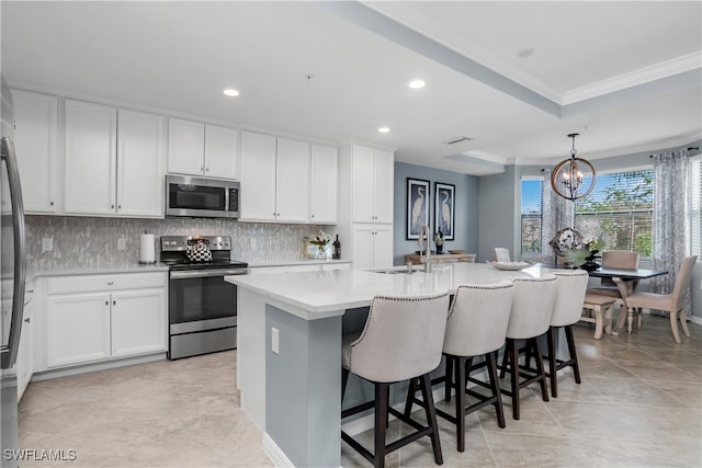 kitchen with white cabinets, an island with sink, decorative light fixtures, a kitchen bar, and stainless steel appliances