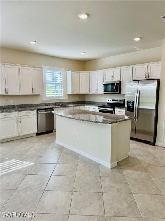 kitchen with white cabinetry, appliances with stainless steel finishes, a kitchen island, and dark stone counters