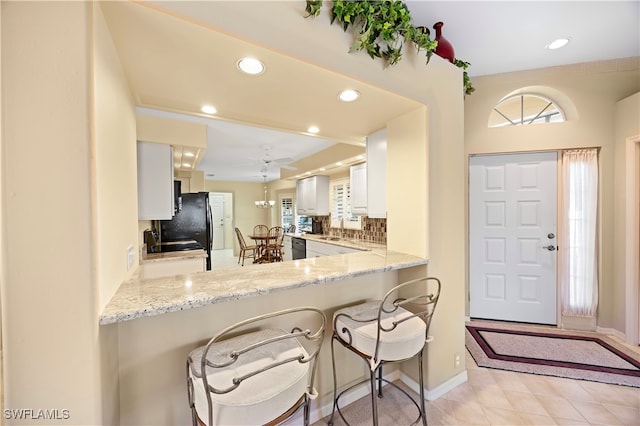 kitchen with sink, light stone counters, kitchen peninsula, decorative backsplash, and white cabinets