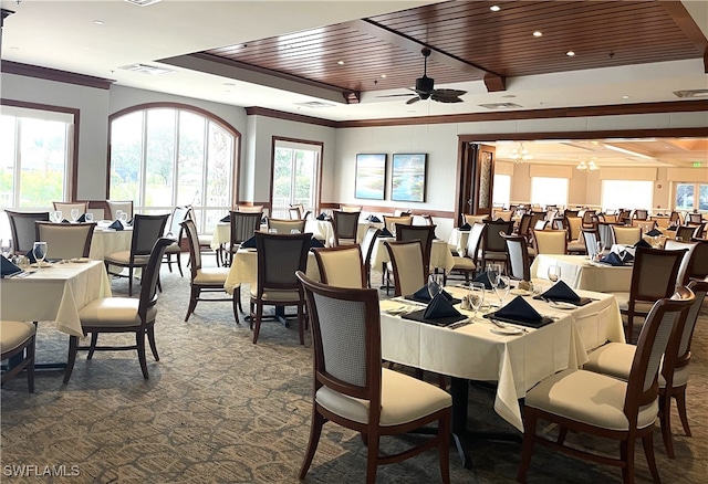 dining space with dark carpet, a raised ceiling, crown molding, wood ceiling, and ceiling fan with notable chandelier