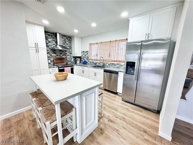 kitchen featuring wall chimney exhaust hood, white cabinetry, stainless steel appliances, and a kitchen breakfast bar