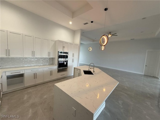 kitchen featuring white cabinets, ceiling fan, a kitchen island with sink, and sink