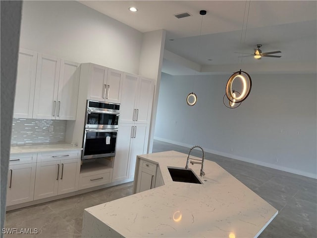 kitchen with pendant lighting, white cabinets, sink, light stone countertops, and double oven