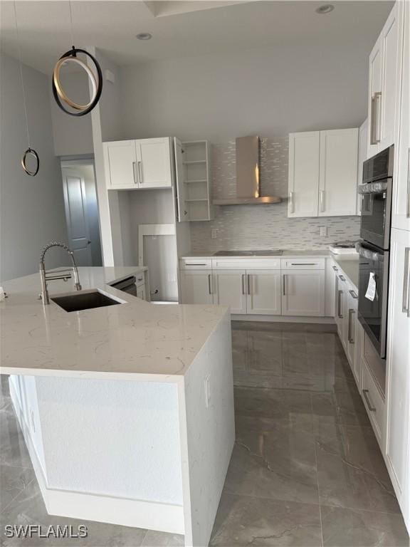 kitchen featuring light stone counters, wall chimney range hood, sink, decorative light fixtures, and white cabinetry