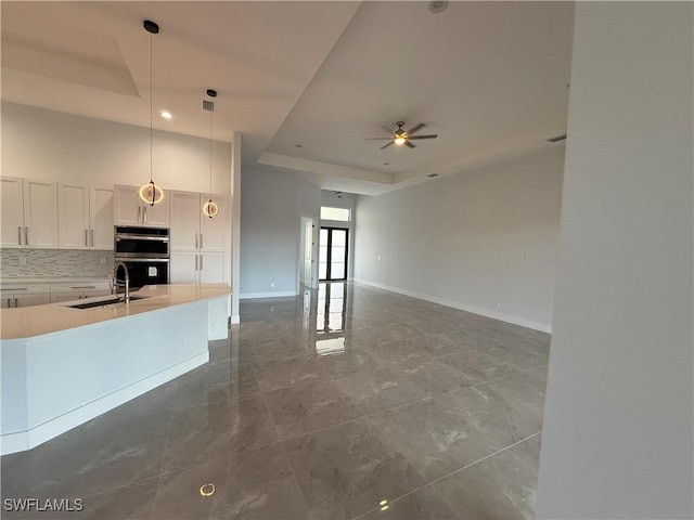 kitchen featuring white cabinets, sink, hanging light fixtures, ceiling fan, and a tray ceiling