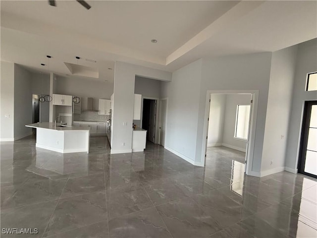 kitchen featuring a kitchen island with sink, a high ceiling, white cabinets, wall chimney range hood, and sink