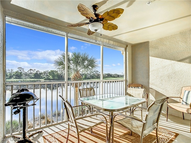 sunroom with ceiling fan and a water view