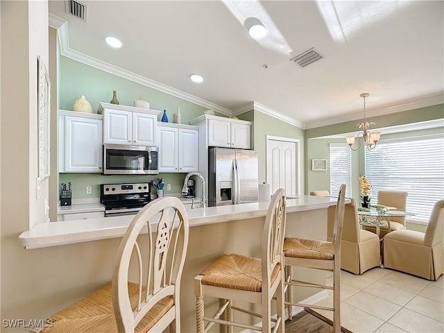 kitchen with a kitchen bar, stainless steel appliances, crown molding, a chandelier, and white cabinetry