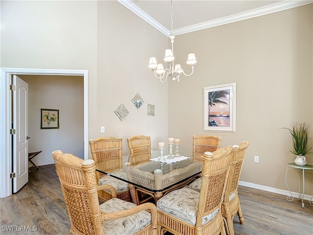 dining area with wood-type flooring, a towering ceiling, an inviting chandelier, and ornamental molding