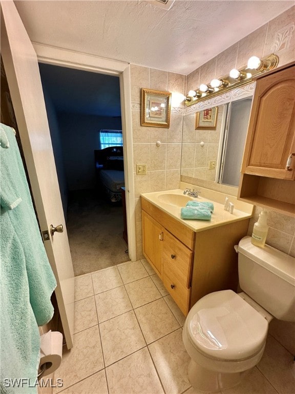 bathroom with a textured ceiling, vanity, tile walls, tile patterned flooring, and toilet