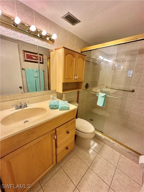 bathroom featuring tile patterned flooring, a textured ceiling, toilet, a shower with door, and vanity