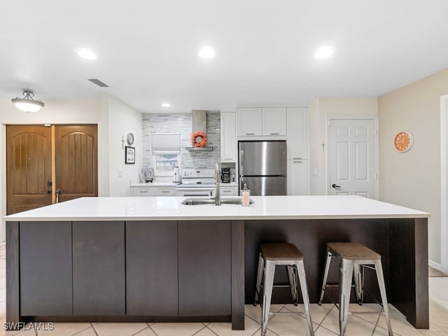 kitchen featuring a large island, stainless steel refrigerator, white range, white cabinets, and wall chimney exhaust hood