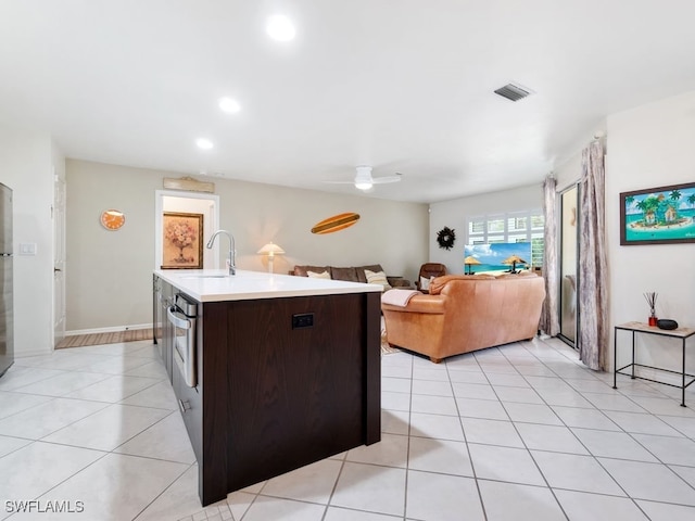 kitchen featuring an island with sink, sink, dark brown cabinetry, and light tile patterned floors