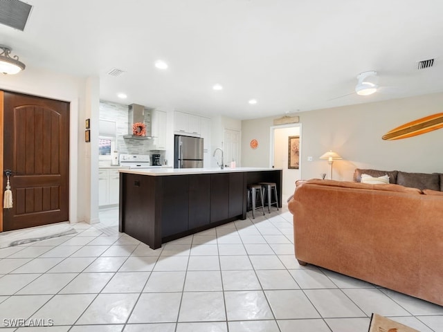 kitchen featuring white cabinets, light tile patterned floors, wall chimney range hood, stainless steel refrigerator, and a spacious island