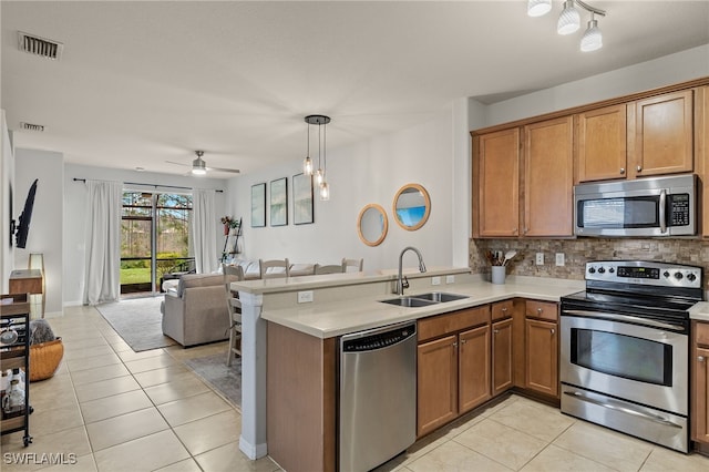 kitchen with kitchen peninsula, sink, tasteful backsplash, light tile patterned flooring, and appliances with stainless steel finishes